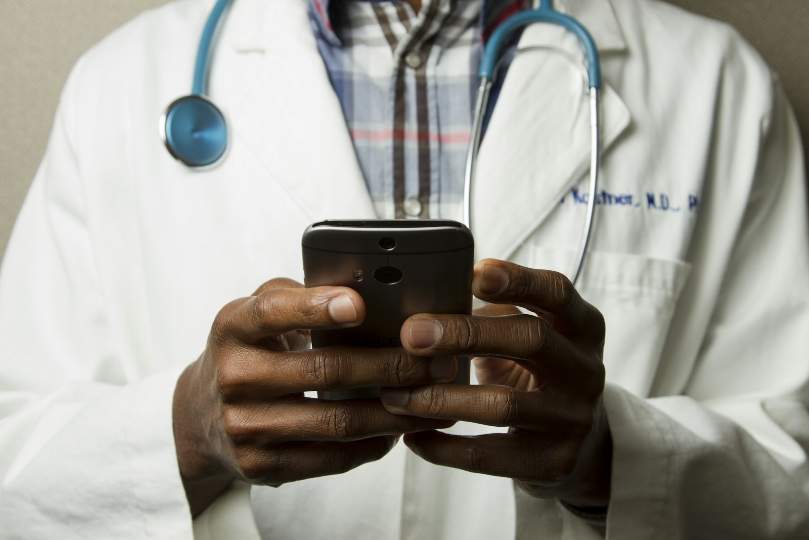 Black clinician using a phone while wearing a lab coat and stethoscope
