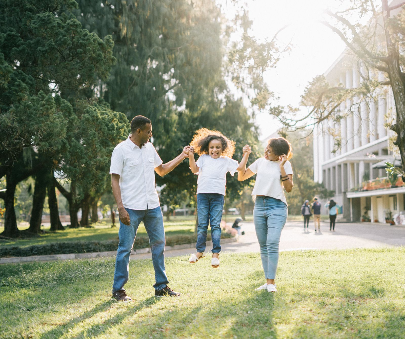 Black parents joyfully swinging their young daughter outdoors
