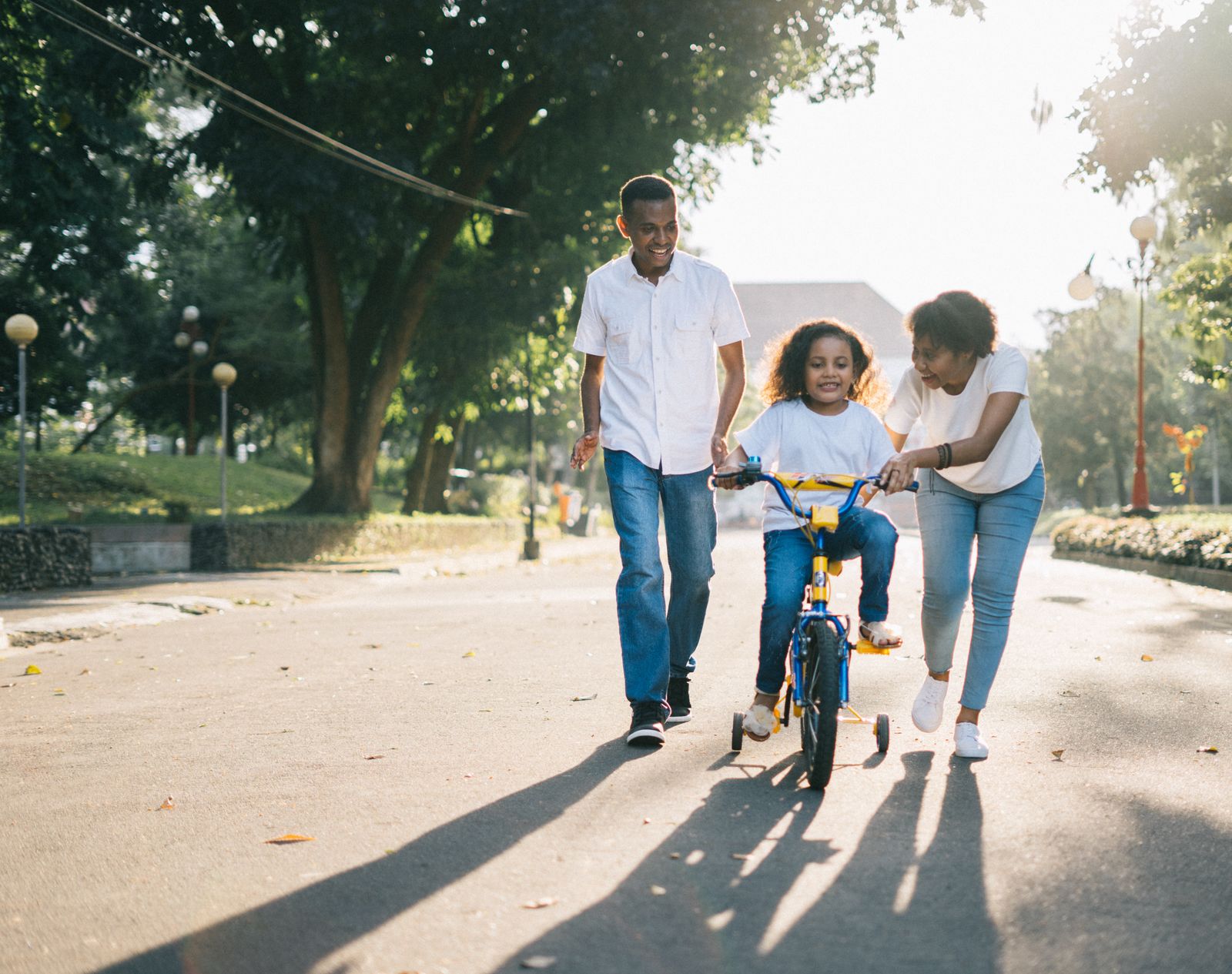 Black family helping their child ride a bicycle in a sunny park