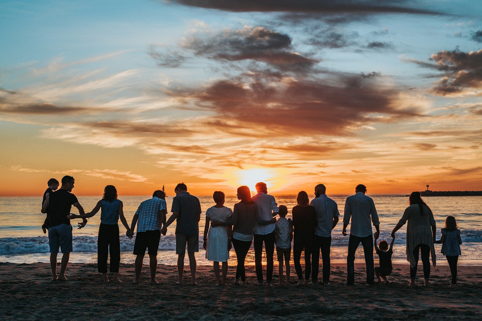 A diverse community standing together on a beach at sunset